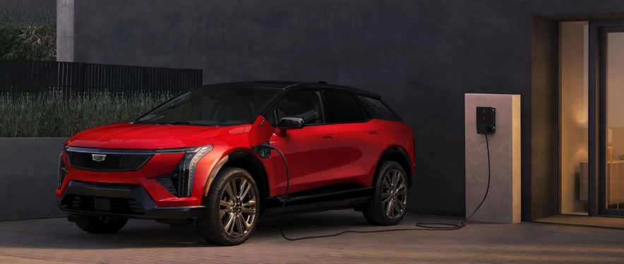 Red Cadillac LYRIQ EV parked and charging at a wall-mounted station outside a modern building.