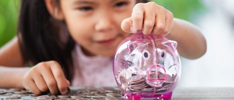 Little girl adding money to a piggy bank