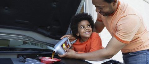 Father showing son how to put motor oil in a vehicle