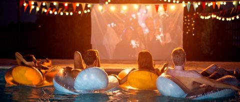 Four friends float in a pool while watching a movie on a projector