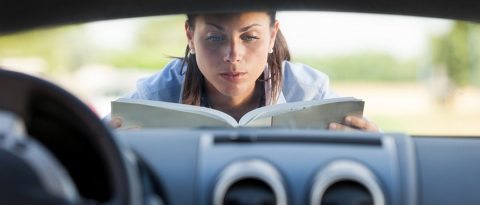Woman reading manual on hood of new car