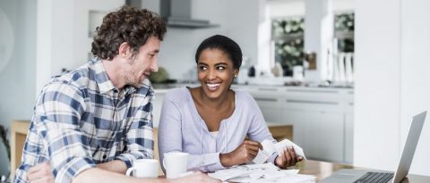 A smiling couple looks through receipts at their kitchen table.