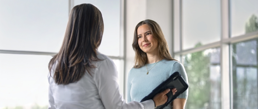 Woman listening while a GM salesperson tells her about the GM Rewards program using a tablet.